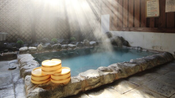 A hot spring area with a stone pool, wooden benches, and a wooden cabin structure.