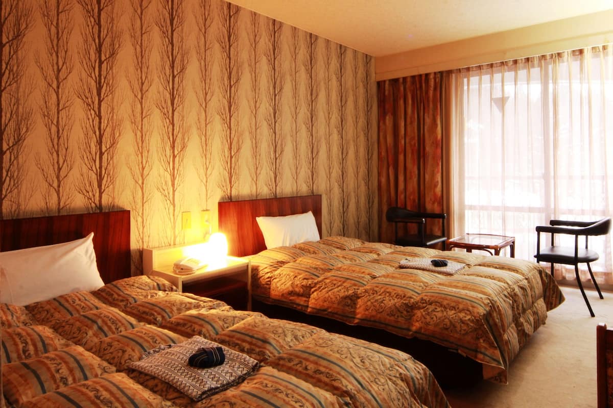 Een hotelkamer met twee bedden, een bureau, een stoel en een groot raam met gordijnen.