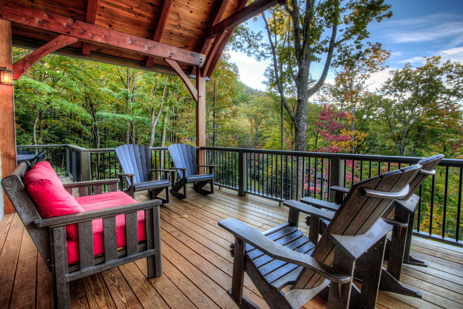 Une terrasse en bois, agrémentée de chaises Adirondack et d’un banc rouge avec coussin, donnant sur une zone boisée.