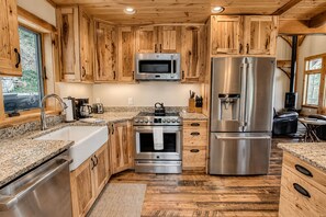 A kitchen with wooden cabinets, stainless steel appliances, granite countertops, and a wood floor. - Rustic Timber | 5-Bedroom Pet Friendly Black Mountain Retreat with Views (Fairview)