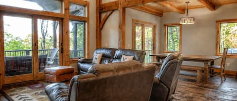 A spacious living room with a leather sofa, a dining table, and a chandelier.