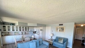 Un ambiente compatto con angolo cottura, un divano blu, un tavolino da caffè e un tappeto decorato.