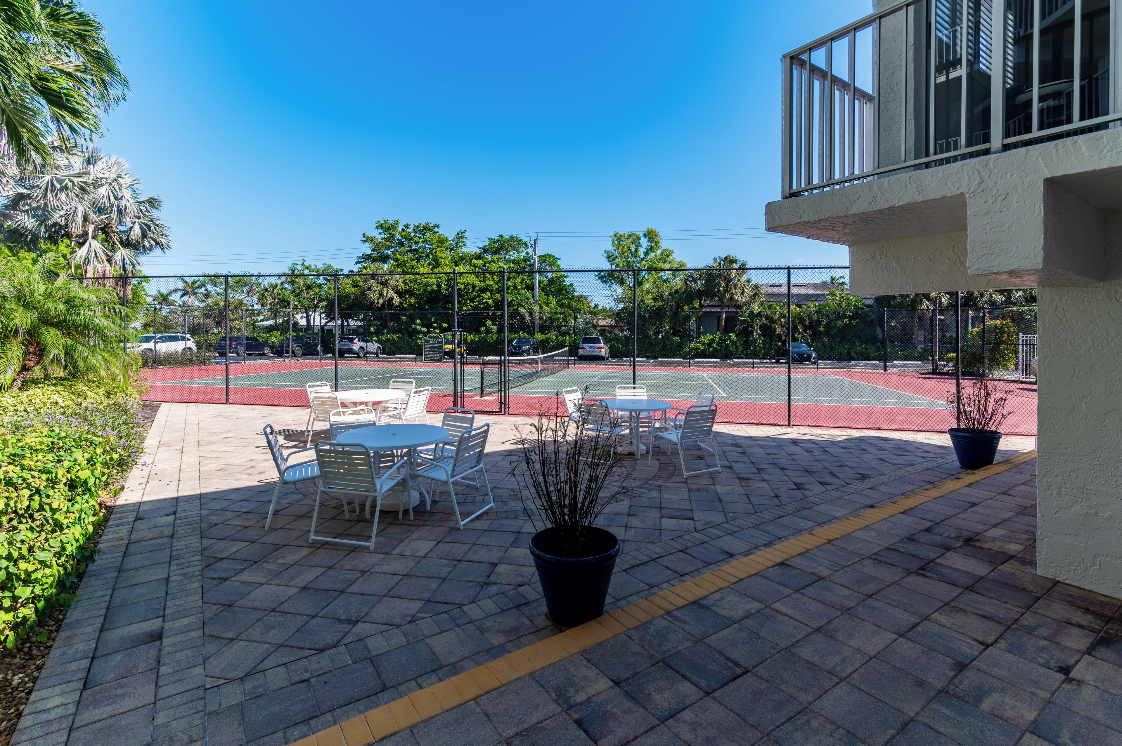An outdoor patio area with tables and chairs, a tennis court, and a building with a balcony.