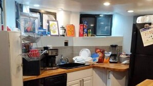 Una cucina compatta con mobili bianchi, lavastoviglie, lavello e frigorifero.