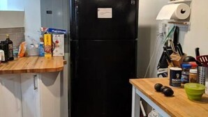 Una cucina compatta con frigorifero nero, piano di lavoro in legno e un piccolo angolo ristoro con tavolo e sedie bianche.