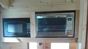 A compact kitchen with a microwave, stove, and sink. There is a small seating area with a window above the sink.