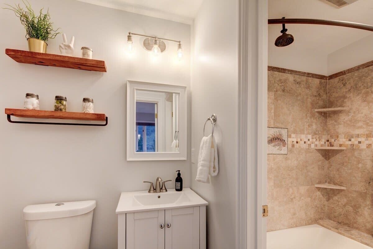 Un bagno con il water, un lavandino, uno specchio, mensole con barattoli e una zona doccia.