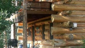 A log cabin with a balcony, a stone foundation, and outdoor seating. - Spectacular Large Group Accommodations with Gallatin River access! (Bozeman)