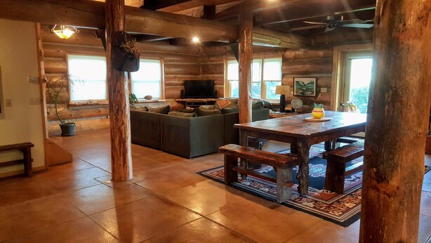 A rustic interior with a wooden dining table, a sofa, and a television in a log cabin-style room. - Spectacular Large Group Accommodations with Gallatin River access! (Bozeman)