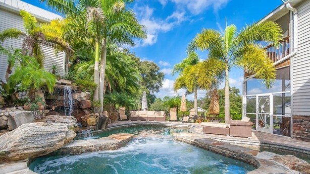 Une piscine agrémentée d’une cascade, entourée de palmiers et dotée d’une terrasse en pierre.