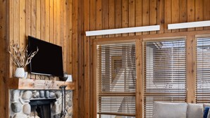 Una sala de estar acogedora con chimenea de piedra, paredes de madera, un televisor de pantalla plana y una zona de estar confortable.