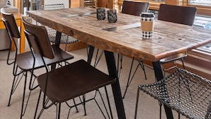 Un comedor con una mesa de madera, sillas de metal y una lámpara colgante de alambre original.
