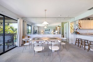 Une cuisine moderne dotée d’un grand îlot central, de chaises blanches et d’une porte vitrée donnant sur un balcon.