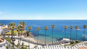 Un hotel frente al mar con vista a la playa, palmeras y un cielo azul despejado.