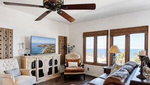 Una sala de estar con ventilador de techo, televisor, sofá, sillón y aparador.
