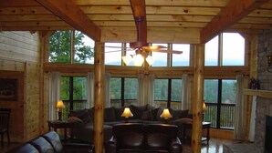 Amplia sala de estar con un gran techo de madera, chimenea y múltiples ventanas con vistas al exterior.