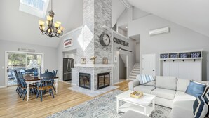 Un salon spacieux avec une cheminée, un coin repas avec une table et des chaises en bois, un canapé agrémenté de coussins décoratifs et un escalier menant à un autre niveau.