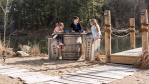 A wooden dock with a wooden barrel labeled "CRAB" and "LOBSTER" in front of a lake, surrounded by trees. - Castaway lake side canvas cottage scene (Jasonville)