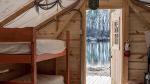 A cabin with a wooden interior, a bunk bed, a door leading to a dock by a lake, and a lantern hanging from the ceiling. - Castaway lake side canvas cottage scene (Jasonville)