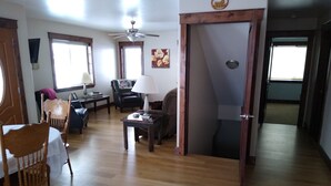 Een ruime woonkamer met houten vloer, een plafondventilator, een eettafel met stoelen, een bank en een salontafel.