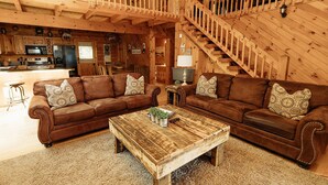 A cozy log cabin interior with a wooden staircase, a living room with two brown leather sofas and a coffee table, and a kitchen area with modern appliances. - "Rustic Relaxation" Lodge with a Gorgeous View!!! (Sevierville)