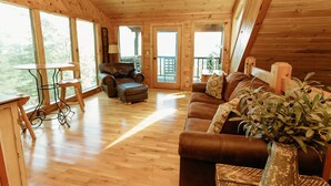 A wooden cabin interior with a wooden floor, a leather sofa, a leather armchair, a small table, and a ceiling fan. - "Rustic Relaxation" Lodge with a Gorgeous View!!! (Sevierville)