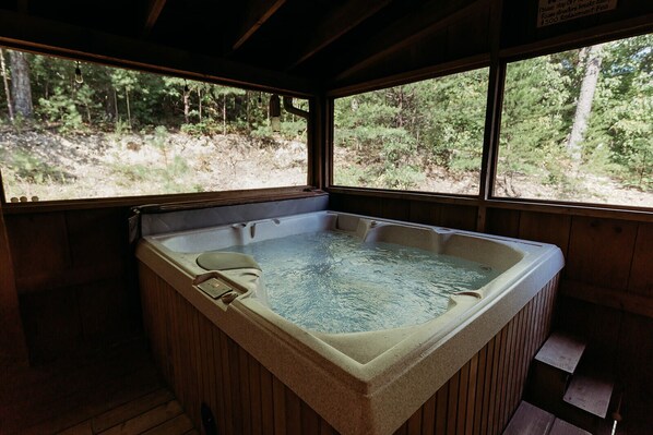 A hot tub with a wooden interior and a view of a forest through large windows.