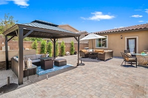 Relax in style with a sofa, dining table, and small table amidst a beautifully paved patio under a shaded pergola.