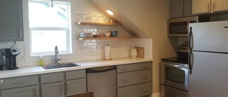 A kitchen with grey cabinets, a dishwasher, a sink, and a refrigerator.