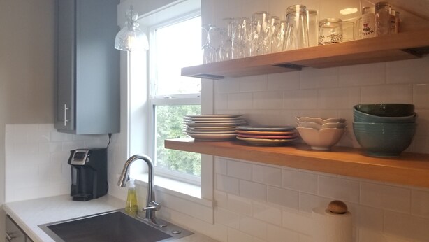 A kitchen with a sink, a faucet, and a window. There are shelves with glassware and plates.