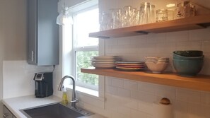A kitchen with a sink, a faucet, and a window. There are shelves with glassware and plates. - Near University & Downtown Missoula: Ideal Spot – Now Offering Mid-Term Rentals (Missoula)