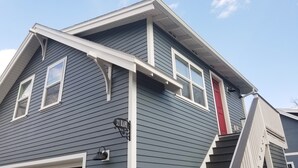 A residential house with a dark gray siding, white trim, and a red door.