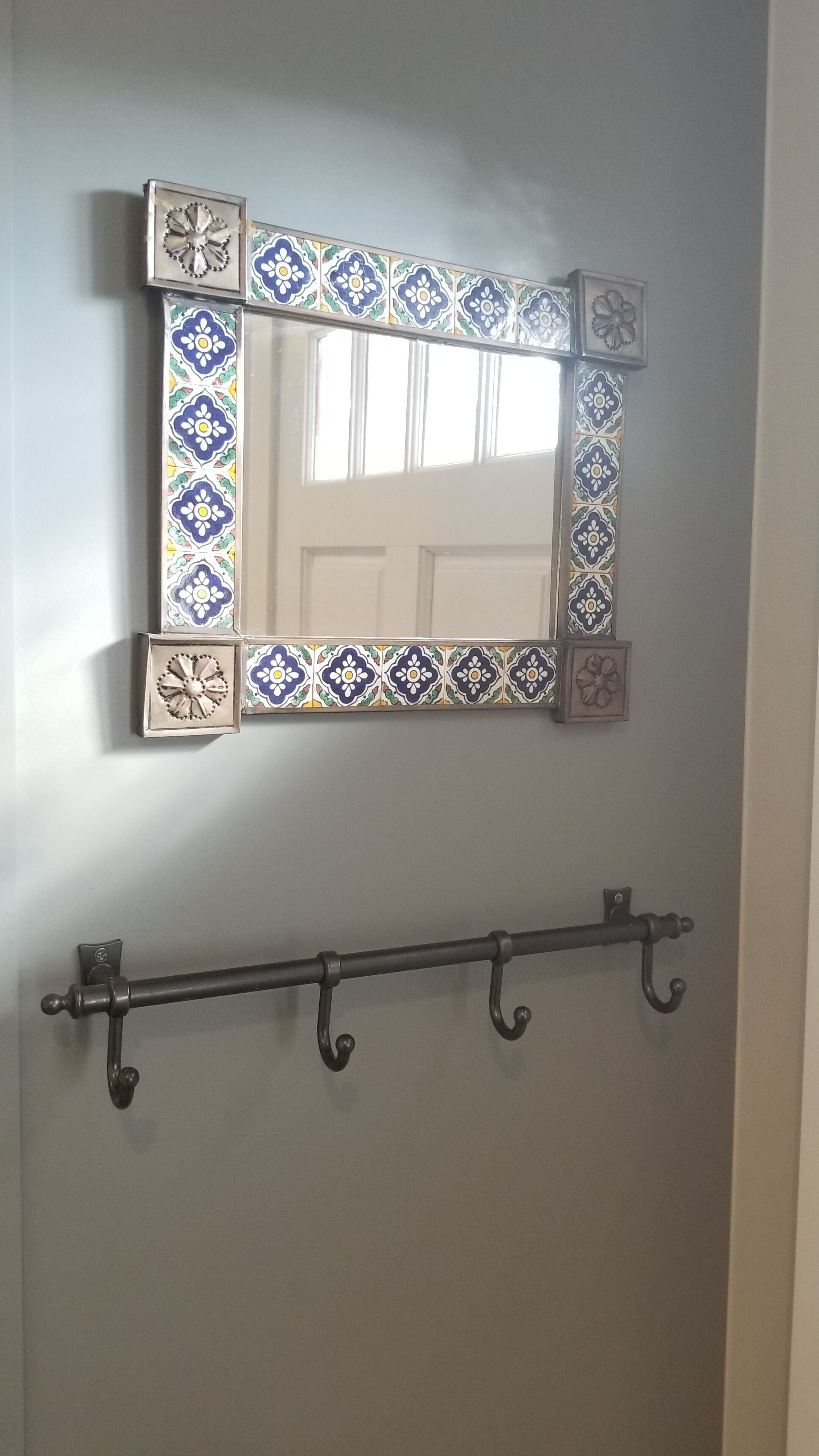 Un baño con un espejo decorativo y un perchero metálico.