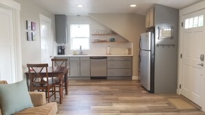 A compact kitchen with a dining area, wooden flooring, and a refrigerator.