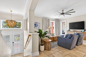 A spacious living room with a ceiling fan, a large flat-screen TV, and a comfortable seating area.