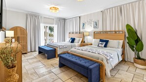 Ein Hotelzimmer mit zwei Betten, einem hölzernen Kopfteil, einer Bank, einer großen Pflanze und Blick ins Freie.