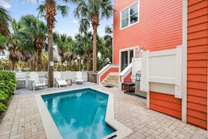 A swimming pool with white chairs, a red building, and palm trees.