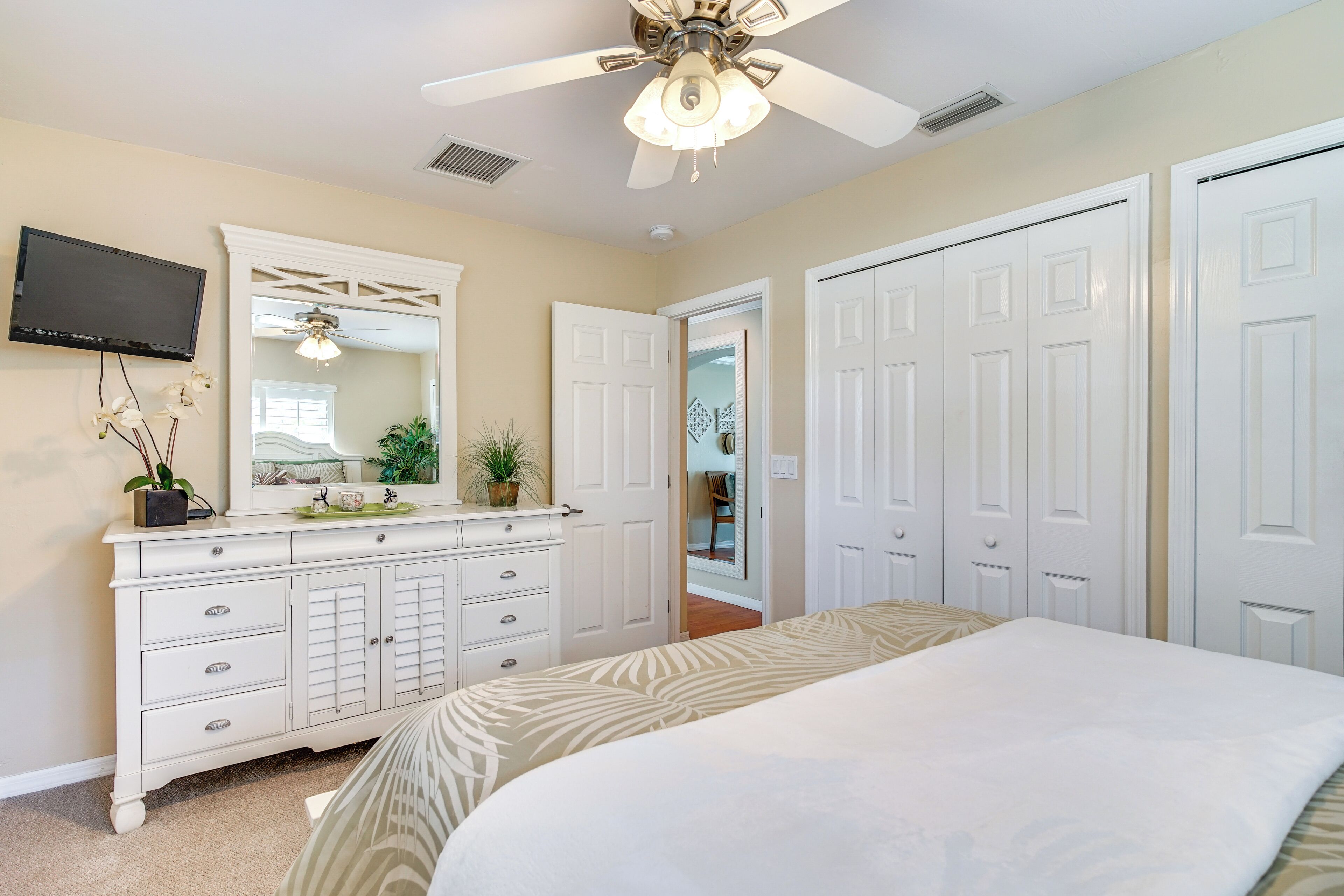 A bedroom with a bed, a dresser, a ceiling fan, a TV, and white doors.