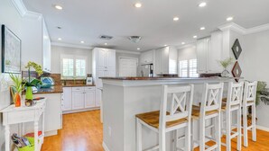 Una cocina amplia con armarios blancos, una isla central con taburetes y un techo luminoso y bien iluminado.