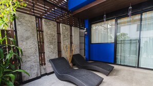Een moderne buitenlounge met twee loungestoelen, een potplant en een bamboeplementenarrangement.