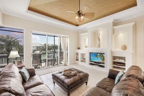 A spacious living room with a large television, leather sofas, a fireplace, and a ceiling fan. - Waterfront Home | Pool, Spa & Direct Boating Access (Marco Island)
