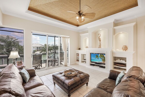 A spacious living room with a large television, leather sofas, a fireplace, and a ceiling fan.