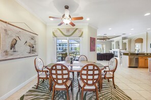 A dining area with a large table and chairs, a ceiling fan, and a view through glass doors to the outside.