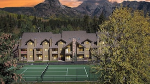 Un lodge con campo da tennis, circondato da montagne e alberi.