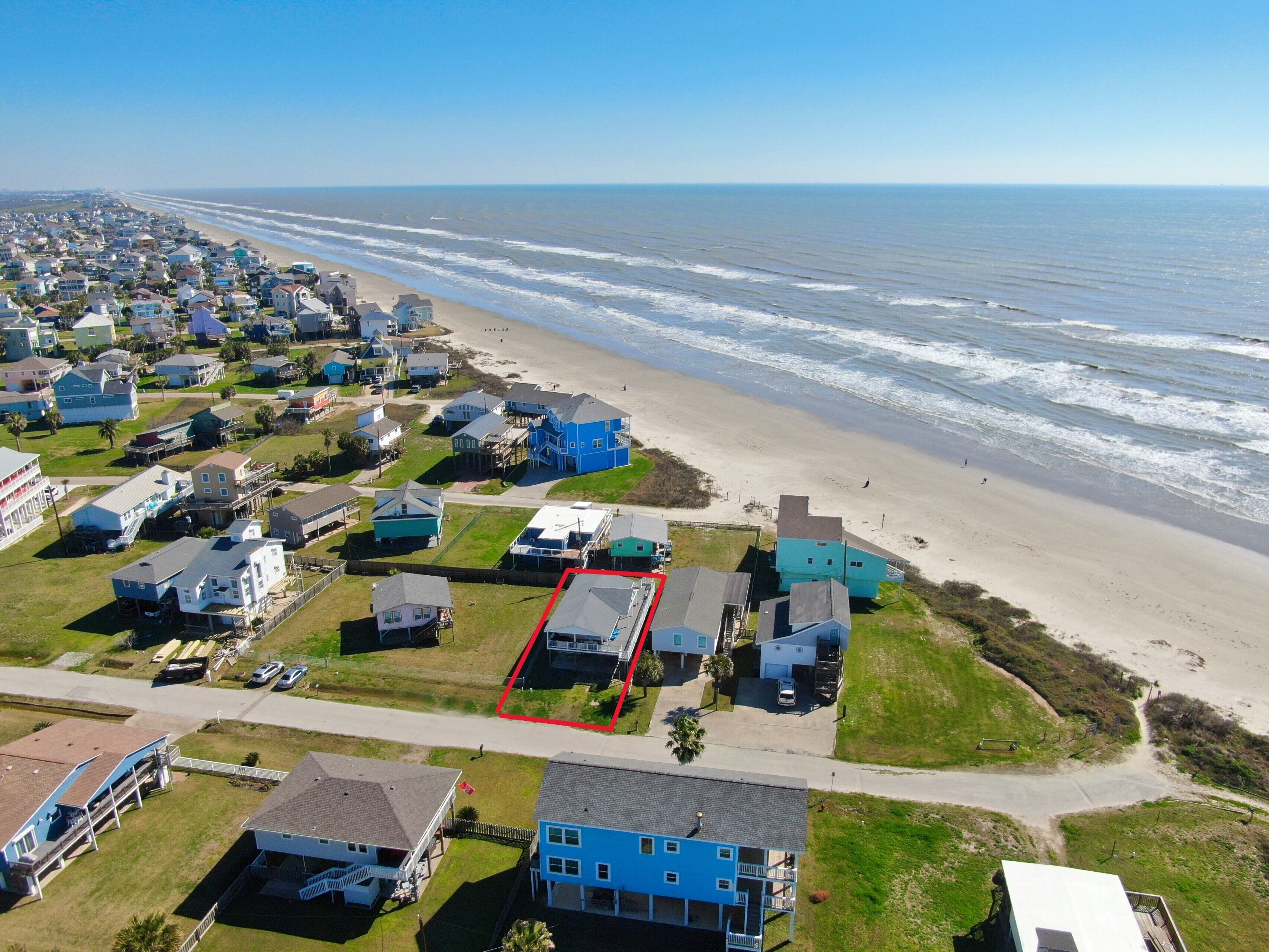 Vue aérienne d’une zone résidentielle côtière, avec des maisons, une plage et un ciel dégagé.