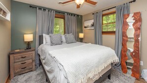 Une chambre à coucher comprenant un lit, deux tables de chevet, un ventilateur de plafond et un grand miroir.