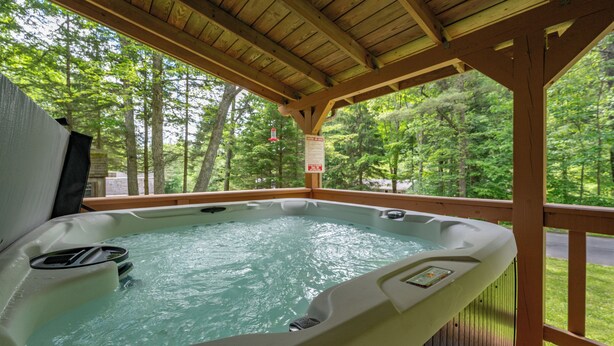 Un bain à remous situé sous une terrasse en bois, avec vue sur une zone boisée.