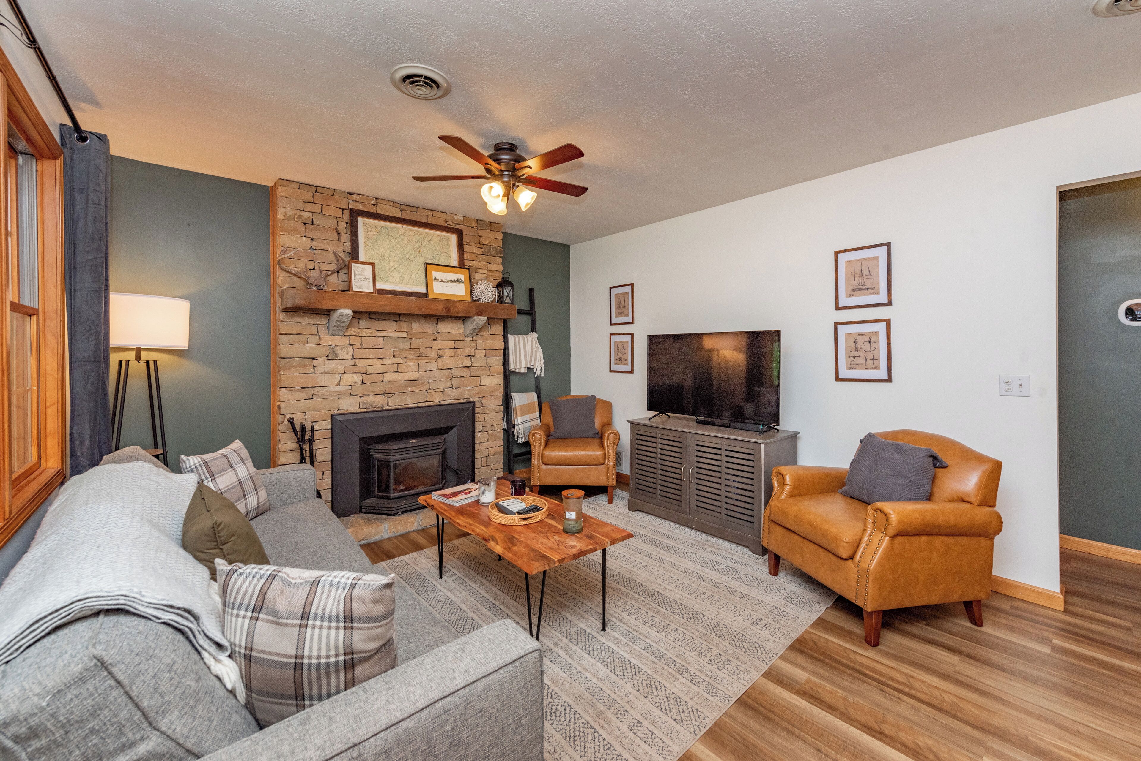 A cozy living room with a fireplace, a ceiling fan, a television, and comfortable seating.