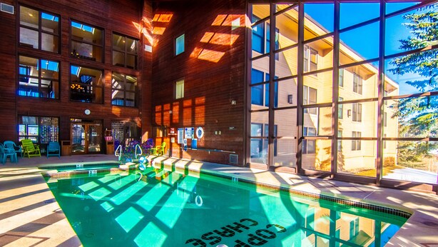 A swimming pool with a sunlit interior, surrounded by large windows and a wooden building facade. - Brian Head Royal Prince Suite, Pool & Jacuzzi, Ski-I/O, 3 BR +, 2 Bath, Sleep 14 (Brian Head)