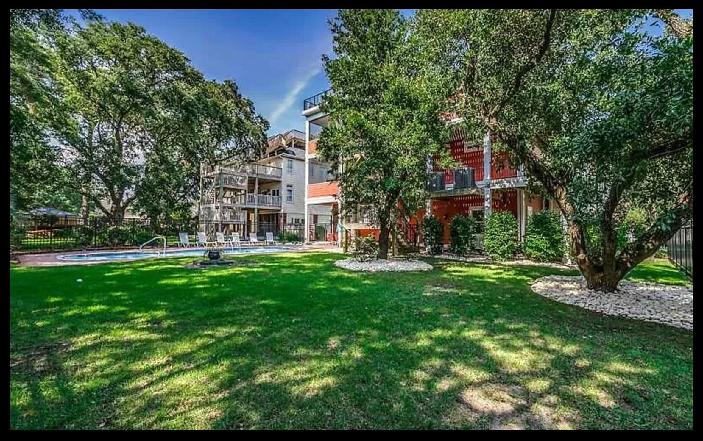 A two-story building with a swimming pool, surrounded by lush greenery and trees.